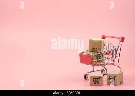 Concetto di shopping - cartoni o scatole di carta nel carrello di shopping rosso su sfondo rosa. I consumatori di shopping in linea possono acquistare da casa e servizio di consegna. Foto Stock