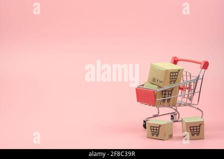 Concetto di shopping - cartoni o scatole di carta nel carrello di shopping rosso su sfondo rosa. I consumatori di shopping in linea possono acquistare da casa e servizio di consegna. Foto Stock