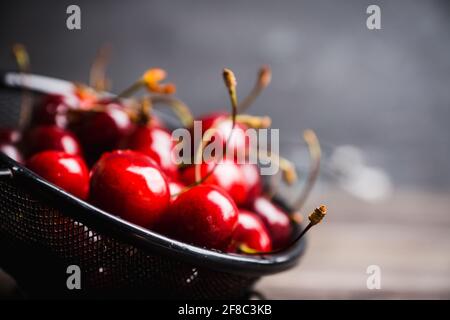 Ciliegie mature e succose in setaccio di metallo nero su fondo rustico scuro. Messa a fuoco selettiva. Profondità di campo poco profonda. Foto Stock