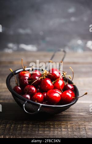 Ciliegie mature e succose in setaccio di metallo nero su fondo rustico scuro. Messa a fuoco selettiva. Profondità di campo poco profonda. Foto Stock