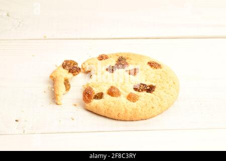 Un biscottino rotondo fragrante, fresco, gustoso, dolce, sbriciolato con uvetta, macro, su sfondo di legno naturale dipinto. Foto Stock