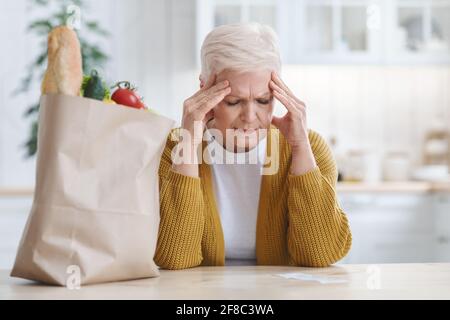 Donna anziana sconvolto che controlla il conto della spesa in cucina Foto Stock