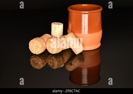 Diversi tappi di vino marrone chiaro con un bicchiere di ceramica, primo piano su sfondo nero. Foto Stock