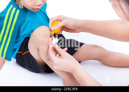 Piccolo ragazzo asiatico che guarda la gamba, Madre fornisce pronto soccorso, sparare in studio, su sfondo bianco Foto Stock