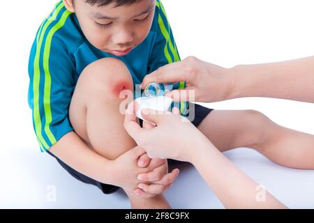 Piccolo ragazzo asiatico che guarda la gamba, Nurse fornisce pronto soccorso, sparare in studio, su sfondo bianco Foto Stock