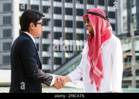 L'uomo arabo e l'uomo d'affari scuotono le mani durante un incontro d'affari. Moderno sfondo cittadino. Multiculturale, multietnico. Foto Stock