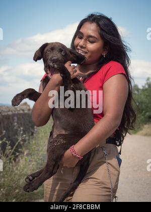 Allegra donna asiatica che gioca con un cucciolo labrador di cioccolato di tre mesi. Foto Stock