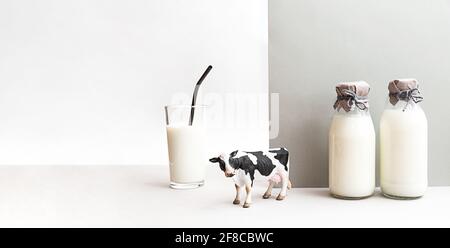 Bottiglie di latte fresco, una figurina di una mucca e un bicchiere di latte su fondo grigio chiaro. Minimalistica vita morta del latte, spazio di copia. Foto Stock