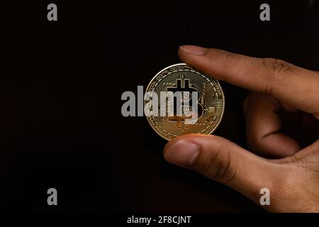 Primo piano su una moneta d'oro con il simbolo della moneta di bit in mano. Moneta di criptovaluta con mano giovane, monete di denaro digitali, BTC Foto Stock