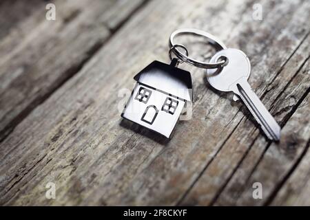 Chiave di casa su una casa portachiavi sagomato poggiante su assi di legno concept per il settore immobiliare, casa mobile o locazione Foto Stock
