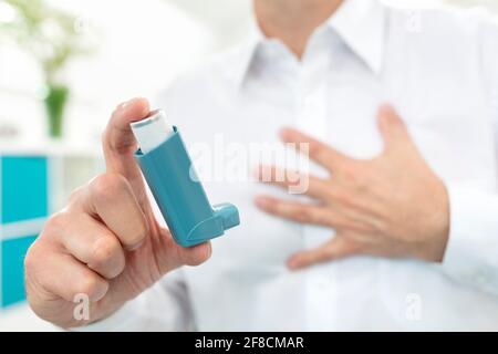 Uomo che usa un inalatore di asma blu con difficoltà respiratorie Foto Stock