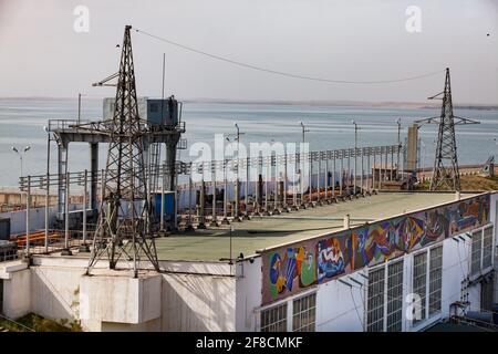 Impianto idroelettrico di Shardara. Diga, edificio principale, autobus elettrici e gru a portale con cabina. Deposito di acqua di Shardara sullo sfondo. Kazakistan. Foto Stock