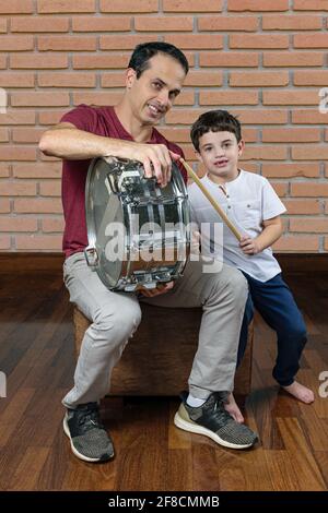 Padre (44 anni) insegnando a suo figlio (7 anni) le prime lezioni di batteria, foto 1. Muro di mattoni sfondo. Foto Stock