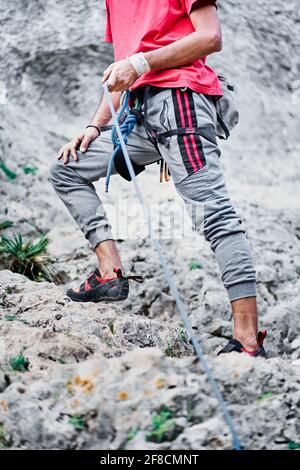 Primo piano di un uomo con l'imbragatura di arrampicata e alpinismo che si prepara a salire. Foto Stock