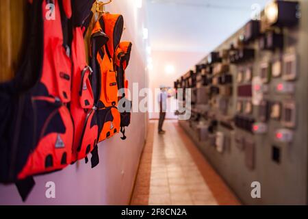 Sala di controllo della centrale idroelettrica di Shardara. Giubbotti di vita arancione (a sinistra) e console sfocata con il lavoratore (a destra). Foto parzialmente sfocata. Kazakistan. Foto Stock