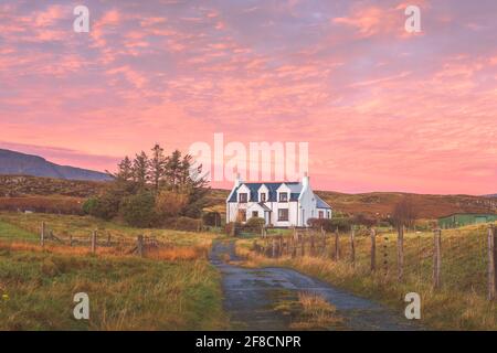 Vibrante, rosa colorato tramonto o cielo sorgere del sole su tradizionale, rurale croft casa in campagna idilliaca a Staffin sull'Isola di Skye, Scott Foto Stock
