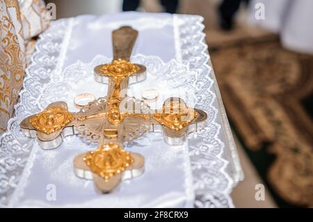 Un paio di anelli di nozze d'oro e una croce di ferro su uno sfondo bianco in una chiesa. Cerimonia nuziale nella chiesa Foto Stock