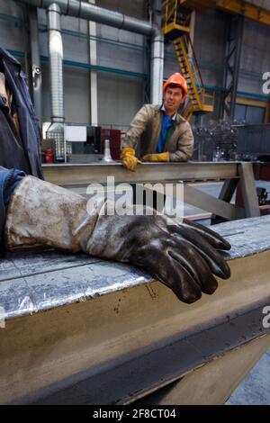 Kazakistan, Nur-sultan. Impianto di costruzione locomotiva. Due lavoratori in officina. Mettere a fuoco il guanto di protezione in pelle scamosciata in primo piano. Foto Stock
