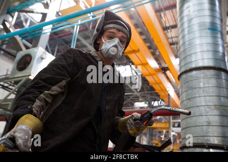 Impianto di costruzione locomotiva. Giovane lavoratore asiatico saldatore in maschera respiratore. Kazakistan, Nur-sultan. Foto Stock