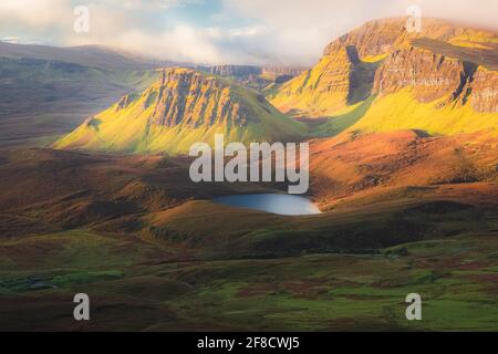 Vivace luce dorata sull'epico paesaggio montano del terreno aspro e contornato di Cleat e Dun Dubh al Quiraing sull'Isola di Skye, Scot Foto Stock