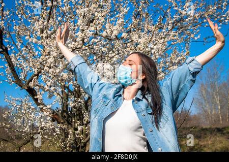 la giovane donna in maschera medica puzza l'albicocca fiorente e godendo la vita Foto Stock