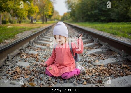 bambina seduta sui binari ferroviari. il bambino gioca sulla ferrovia in foresta Foto Stock