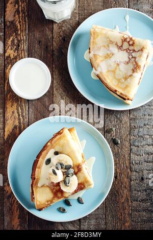 Frittelle sottili con banane e latte condensato in un piatto blu su un tavolo di legno. Foto Stock