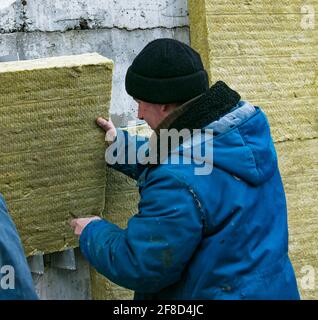 Dnepropetrovsk, Ucraina - 06.04.2021: Un uomo installa uno strato di isolamento termico sotto forma di pannelli di lana minerale. Installazione dei blocchi isover t Foto Stock