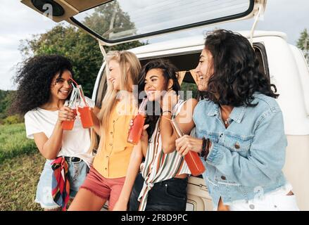 Gruppo di diverse amiche che tostano bottiglie vicino al camper. Quattro donne all'aperto Foto Stock