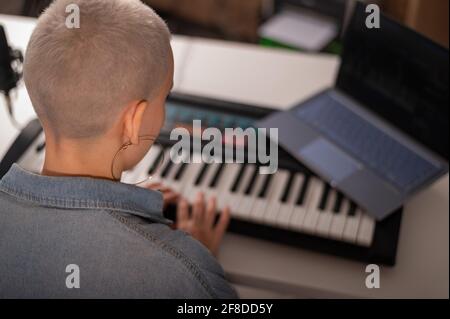 La ragazza suona il pianoforte elettrico e guarda il video. Una donna sta imparando a suonare il sintetizzatore su un laptop Foto Stock
