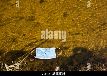 Una maschera medica galleggia lungo il fiume, in un'acqua limpida in una giornata di sole. Foto Stock