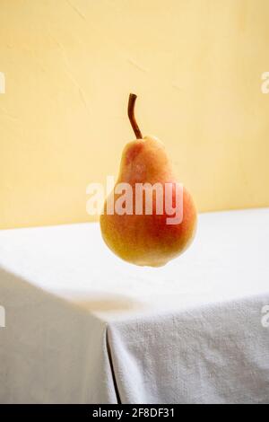 Pera che galleggia nell'aria su un tavolo bianco e sfondo giallo. Foto Stock