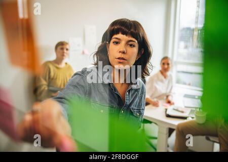 professionista aziendale che guarda le note adesive sulla parete in vetro e crea idee con il team. Giovane donna in piedi in ufficio dietro Glass wal Foto Stock
