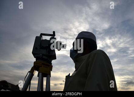 Peshawar. 13 Apr 2021. Un uomo osserva la luna crescente attraverso un telescopio nel Peshawar del Pakistan nord-occidentale il 13 aprile 2021. La luna a mezzaluna del Ramadan è stata avvistata in Pakistan martedì sera e il mese santo inizierà ufficialmente mercoledì, secondo un annuncio ufficiale del comitato di avvistamento della luna del paese. Credit: Saeed Ahmad/Xinhua/Alamy Live News Foto Stock