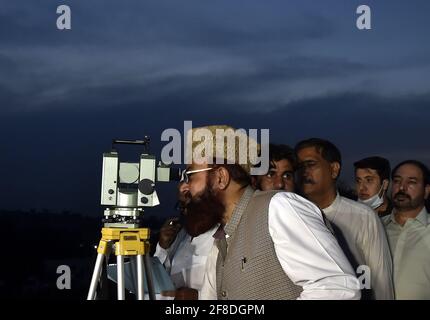 Peshawar. 13 Apr 2021. Un uomo osserva la luna crescente attraverso un telescopio nel Peshawar del Pakistan nord-occidentale il 13 aprile 2021. La luna a mezzaluna del Ramadan è stata avvistata in Pakistan martedì sera e il mese santo inizierà ufficialmente mercoledì, secondo un annuncio ufficiale del comitato di avvistamento della luna del paese. Credit: Saeed Ahmad/Xinhua/Alamy Live News Foto Stock