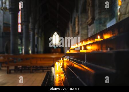 Fuoco selettivo su candela votiva illuminata con luce soffusa e luminoso e sfondo sfocato dell'interno della Cattedrale di St. Marys a Killarney, Kerry, Irlanda Foto Stock