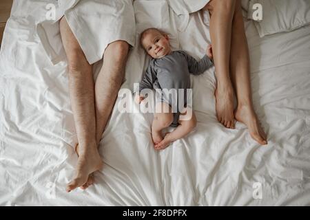 Mattina di felice giovane coppia in accappatoi bianchi con il bambino a letto a casa Foto Stock