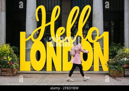 Londra, Regno Unito. 13 aprile 2021. Una donna passa accanto al cartello giallo Hello London a Covent Garden Market. Credito: Waldemar Sikora Foto Stock