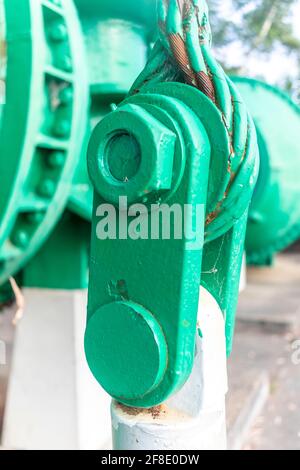 Vista ravvicinata di un vecchio arco di acciaio verde con un dado grande e un cavo in acciaio arrugginito Foto Stock