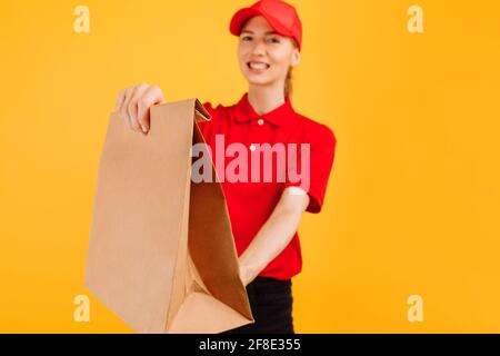 Il deliveryman in uniforme rossa contiene il sacchetto di carta con il cibo, il dipendente femminile in T-shirt rossa e il tappo funziona come corriere, concetto di servizio Foto Stock