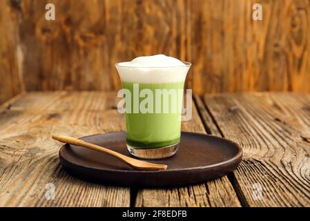 Bicchiere di dalgona matcha latte e cucchiaio su fondo di legno Foto Stock