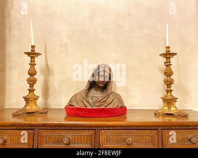 Scultura Vergine Maria, statua su un tavolo di legno circondato da due lunghe candele dorate. CopySpace per il testo Foto Stock