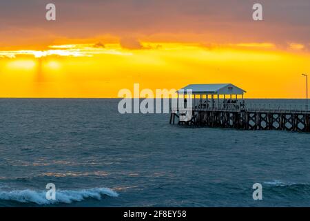 Adelaide, Australia - 11 aprile 2021: Persone che camminano lungo l'Henley Beach Jetty mentre guardano il tramonto drammatico e tempestoso Foto Stock