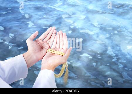 Uomo musulmano che prega con le perle di preghiera sulle sue mani con acqua di fondo calmo Foto Stock