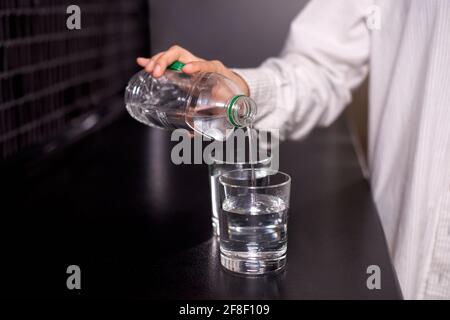 la ragazza sta versando l'acqua dalla bottiglia di plastica in vetro sopra tavolo nero Foto Stock