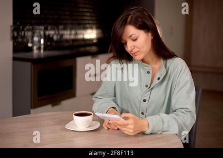 donna usa il tablet a casa con una tazza di caffè o tè in cucina. donna comunica in social network o sito web di riunione Foto Stock