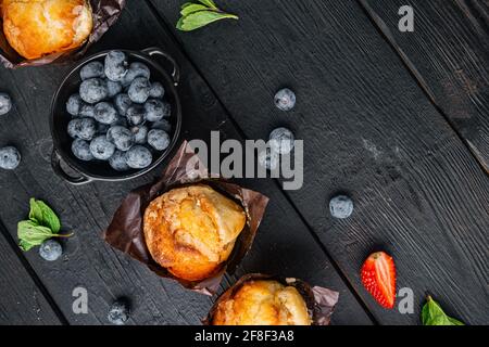 Muffin ai mirtilli con berrie fresca, su sfondo di legno nero, vista dall'alto in piano con spazio per la copia del testo Foto Stock