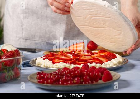 panettiere donna aggiungere un nuovo strato di base meringa in torta di fragole. Torta di fragole fatta in casa con torta di meringa e crema con fragole. Foto Stock