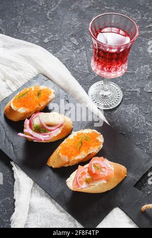 Assortimento di bruschette con baguette, formaggio cremoso, caviale rosso, salmone, aringhe e cipolla serviti su fondo di pietra. Set di antipasti con variou Foto Stock