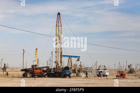 Funziona su un carro di perforazione a olio. Lavoratori, auto, camion e cric di pompaggio nel deserto. Zhanaozen, Kazakistan. Foto Stock